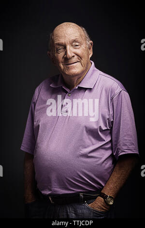 Portrait von älteren Mann mit Händen in den Taschen auf schwarzem Hintergrund stehend Stockfoto