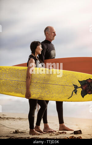 Seitenansicht des Senior Paar mit Surfbrettern auf Ufer am Strand Stockfoto