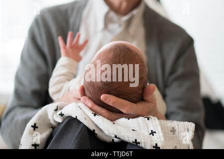 Eine Nacken-nach-unten-Perspektive eines Erwachsenen in einem Hemd mit Kragen, der ein Neugeborenes mit erhobener Hand in der Hand hält. Stockfoto