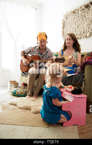 Tochter Klavier spielen, während die Eltern sitzen auf dem Sofa zu Hause Stockfoto