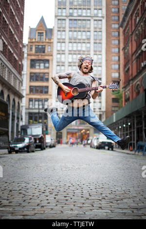 Mann springen während Gitarre spielen auf der Straße in der Stadt Stockfoto