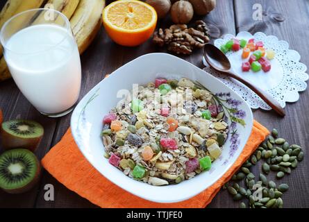 Müsli mit kandierten Früchten und Nüssen mit einem Glas Milch auf einem dunklen Holztisch. Stockfoto