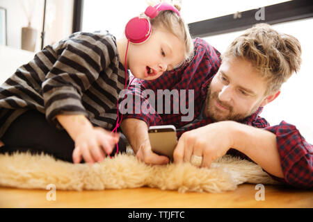 Vater und Tochter auf der Suche nach Handy während auf Fußboden im Home liegen Stockfoto