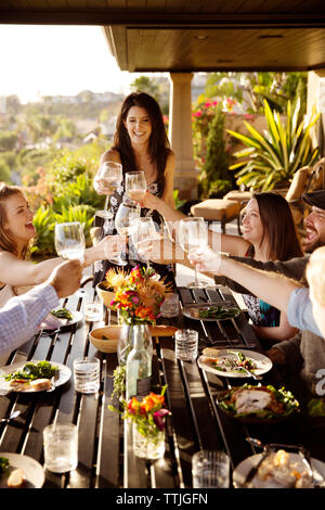 Gerne Freunde toasten Weingläser am Esstisch auf der Veranda Stockfoto