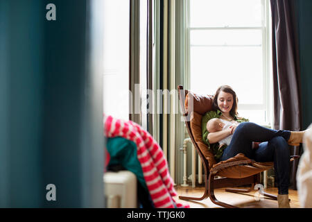 Glückliche Mutter mit Baby Mädchen sitzend auf Stuhl zu Hause Stockfoto
