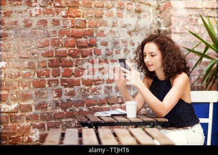 Frau mit Handy während im Straßencafe sitzen Stockfoto