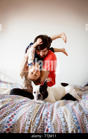 Portrait von Vater spielt mit Tochter und Hund beim Sitzen auf dem Bett gegen die Wand Stockfoto