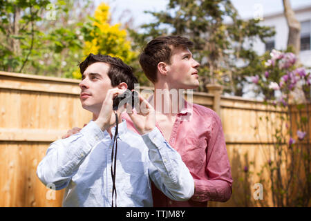 Homosexuelle Männer mit Fernglas suchen beim Stehen im Hinterhof Stockfoto