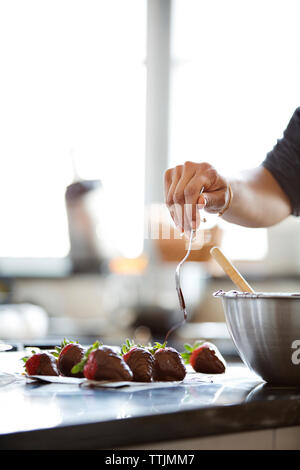 Frau Verbreitung Schokolade auf Erdbeeren Stockfoto