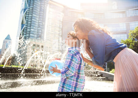 Mutter und Sohn weg schauen, während gegen Brunnen im Park in der Stadt Stockfoto