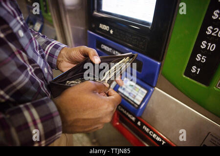 Hohe Betrachtungswinkel der Mann hält Wallet beim Stehen gegen Geldautomaten Stockfoto