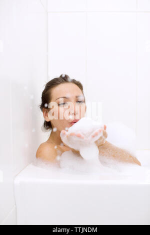 Portrait von Frau blasen Schaum beim Baden zu Hause Stockfoto