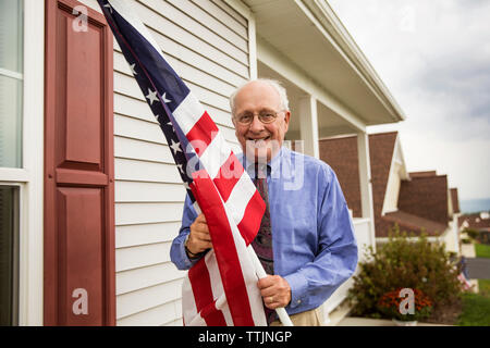 Portrait von älteren Menschen, die amerikanische Flagge, während gegen Haus stehend Stockfoto