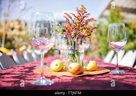 Leere Weingläser mit Früchten und Blumen Vase auf Tisch im Freien bei der Gartenparty Stockfoto