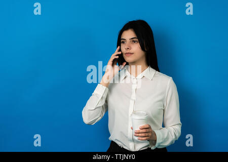 Erfolgreiche Geschäftsfrau mit Smartphone und Kaffee ernsthaft sprechen trhoug Telefon. mittellange Aufnahme Stockfoto