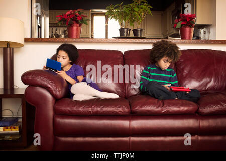 Bruder und Schwester mit Technologien beim Sitzen auf leder Sofa zu Hause Stockfoto