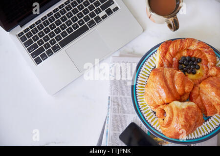 Ansicht von oben mit Croissants in der Platte durch Laptop am Tisch Stockfoto
