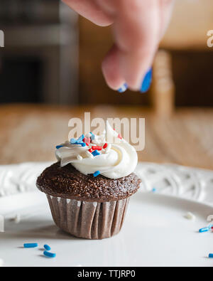 Schokolade mini Cupcake auf einer weißen Platte gesprenkelt mit roten, weißen und blauen Streuseln. Verschwommene Hand über Drop Streuseln. Stockfoto