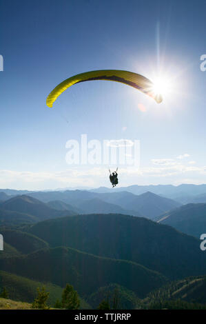 Silhouette person Paragliding über Berge gegen den hellen Himmel Stockfoto