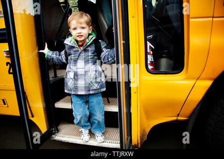 Portrait von süßen Jungen mit Rucksack auf Stufen der Schule Bus Stockfoto