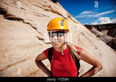 Lächelnde Frau tragen Helm gegen Felsbrocken auf sonnigen Tag stehend Stockfoto