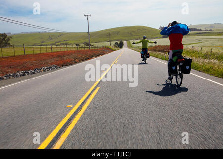 Freunde genießen, während Radfahren auf Landstraße inmitten von Feld gegen Sky Stockfoto