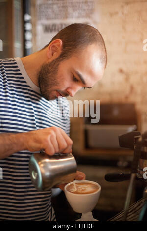 Man gießt Milch im Kaffee im Cafe Stockfoto
