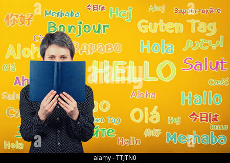 Student Frau mit einem Lehrbuch über gelbe Wand mit Word hallo, in verschiedene Sprachen übersetzt. Gelegenheit für das Lernen. Mehrsprachige te Stockfoto