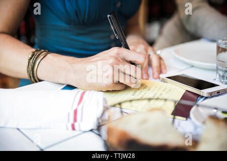 Mittelteil der Frau schreiben auf Notepad während der Sitzung in bar Stockfoto