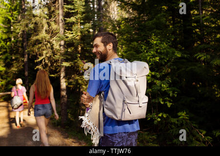 Lächelnder Mann, der Rucksack wandern mit Mutter und Schwester von Bäumen im Wald Stockfoto