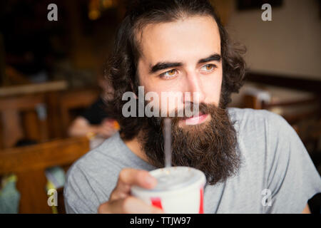 Close-up von nachdenklich Mann mit Bart trinken Cola beim Sitzen im Cafe Stockfoto