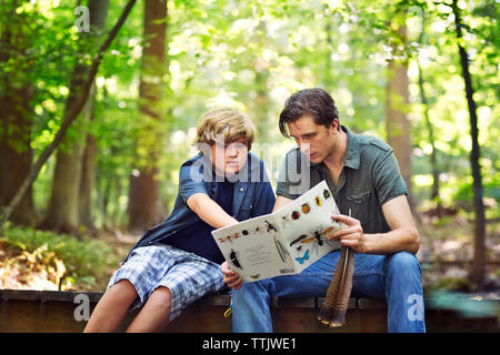 Lehrer und Schüler auf der Suche Buch, während auf der Fußgängerbrücke in Wald sitzen Stockfoto