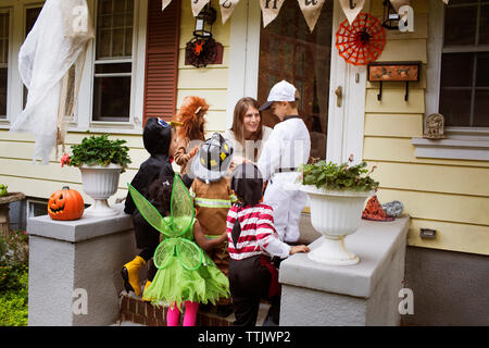 Die Frau spricht zu den Kindern in der Halloween Kostüme während Süßes oder Saures Stockfoto
