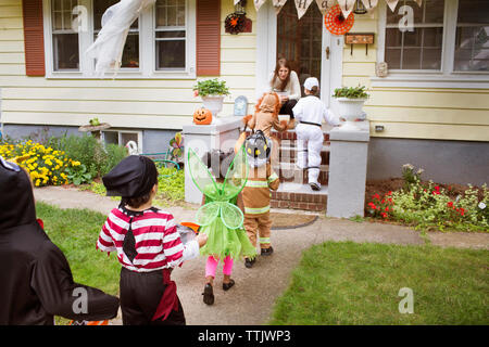 Kinder in Halloween Kostüme zu Fuß in Richtung Frau während der Trick oder das Behandeln Stockfoto