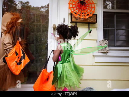 Kinder in Halloween Kostüme stehend an Tür während Süßes oder Saures Stockfoto
