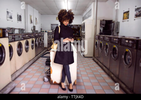 Die ganze Länge der Frau mit Telefon, während im Waschsalon stehen Stockfoto