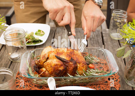 Zugeschnittenes Bild des Menschen Carving gebratenes Huhn an den hölzernen Tisch Stockfoto