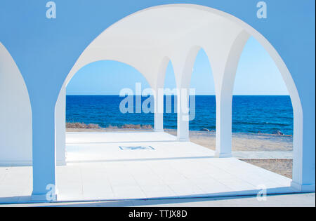 Weiß Ayia Thekla Kapelle mit vielen Bögen in der Nähe von Agia Napa, Zypern. Deep Blue, azurblaues Wasser am Horizont. Erstaunlich Seascape. Warmer Tag im Herbst Stockfoto
