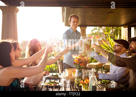 Freunde toasten Weingläser und genießen Sie bei Tisch an der Veranda Stockfoto