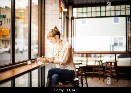 Frau mit smart phone sitzend auf Hocker in bar Stockfoto