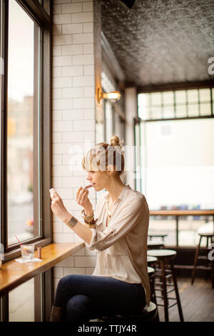 Frau Anwendung Lippenstift sitzend auf Hocker in bar Stockfoto