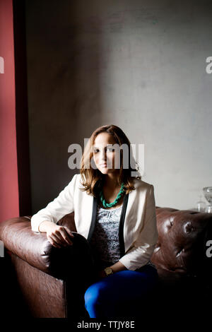 Portrait von zuversichtlich, Frau sitzt auf einem Sessel gegen die Wand im Büro Stockfoto
