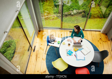 Ansicht von oben, die Glückliche berufstätige Mutter mit Sohn am Tisch gegen Fenster Stockfoto