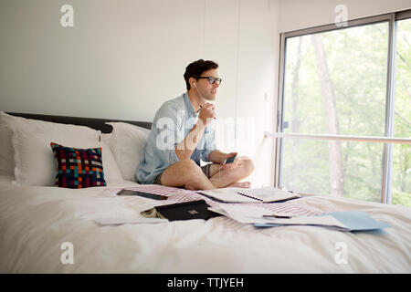 Man spricht über Kopfhörer von Telefon, während auf dem Bett zu Hause arbeiten Stockfoto