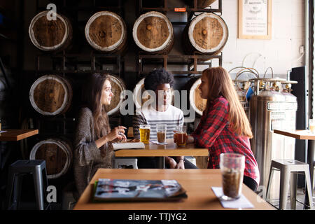 Lächelnd Freunde sprechen, während Bier am Tisch gegen Fässer in Brauerei Stockfoto