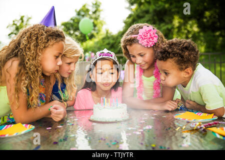 Mädchen bläst Geburtstagstorte Kerzen beim Stehen mit Freunden im Hinterhof Stockfoto