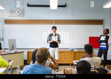 Lehrer an Schüler lesen Papier während in Lektion im Klassenzimmer auf der Suche Stockfoto