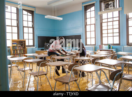 Lehrer und Schüler lesen Buch beim Sitzen im Klassenzimmer Stockfoto