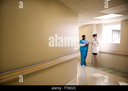 Arzt und Krankenschwester mit Zwischenablage diskutieren, während im Flur stehend Stockfoto