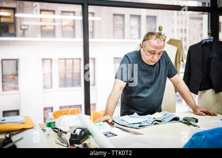 Ernsthafte Fashion Designer bei der Jeans auf den Tisch gegen Glas Fenster in Design Studio suchen Stockfoto